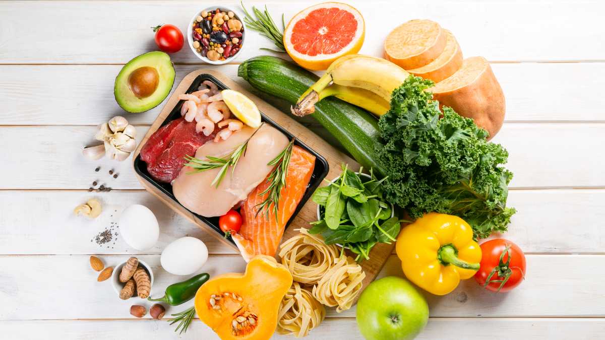 Bancada branca com legumes, frutas, ovos, castanhas, massas e carnes espalhados